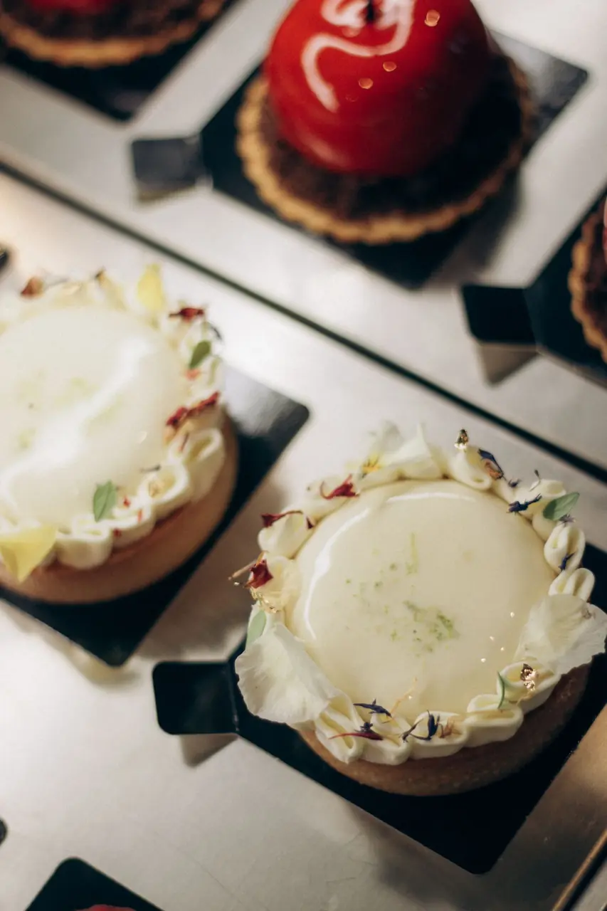 Gourmet tarts with botanical garnishes and piped crème inside the patisserie display
