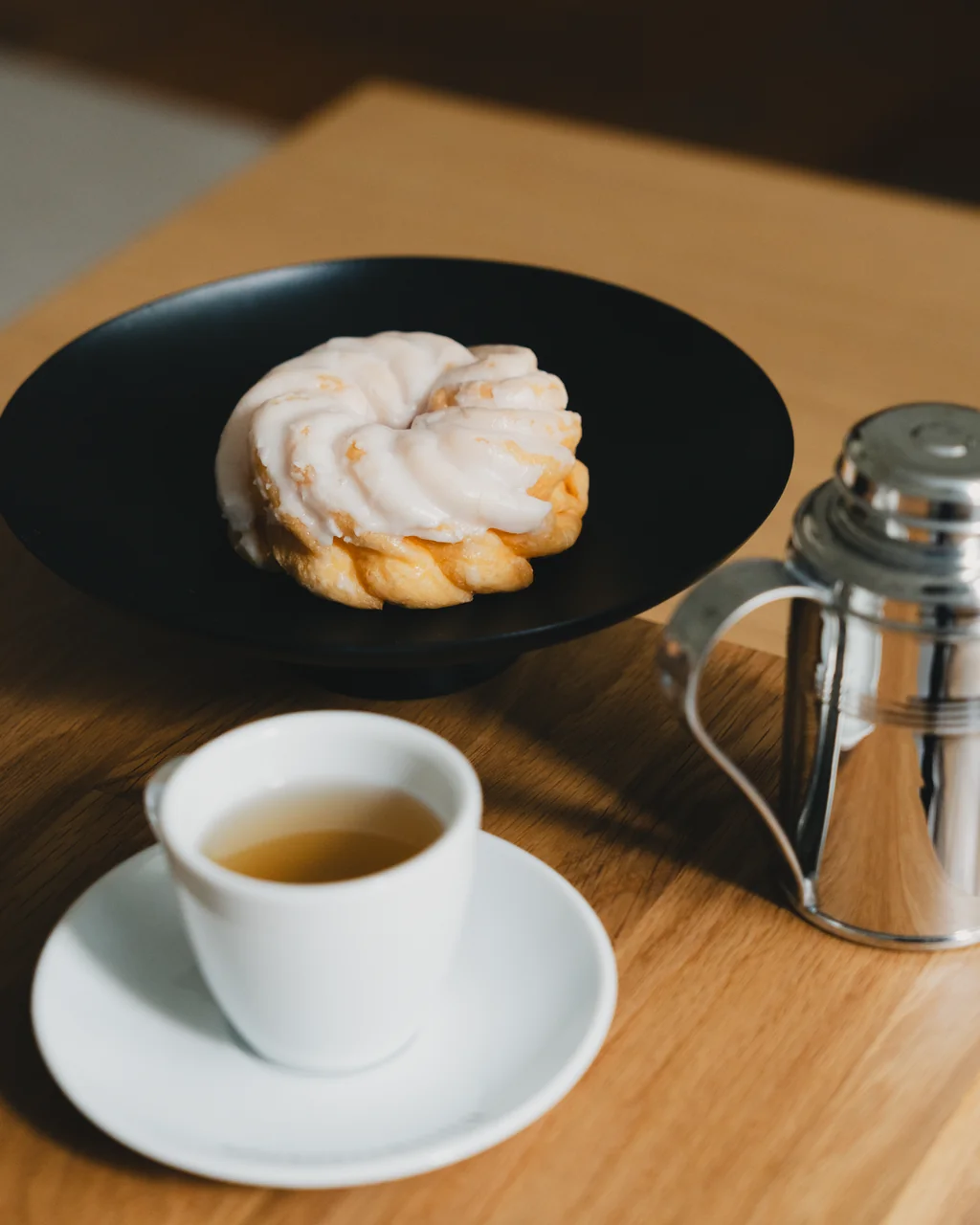 Fine china cup and polished teapot served alongside an artisan patisserie treat on a dark saucer