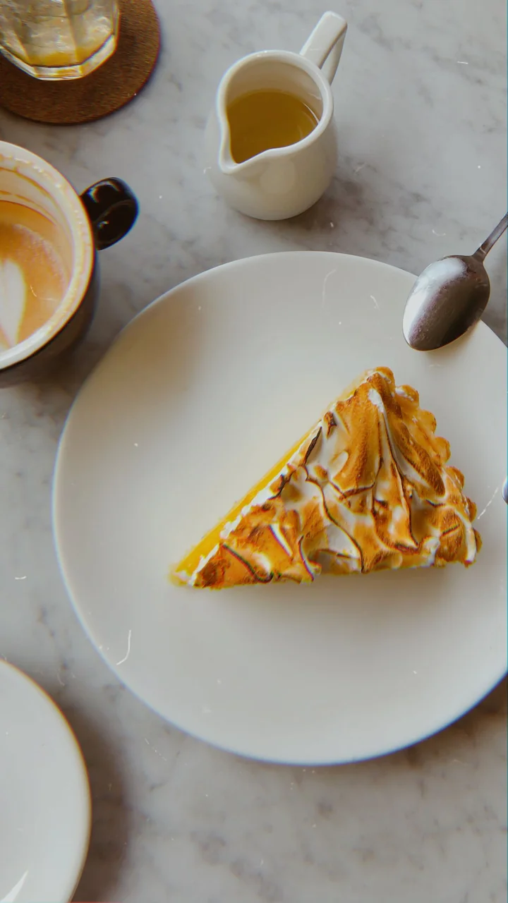Sweet toasted meringue lemon tart served beside freshly prepared coffee on natural marble
